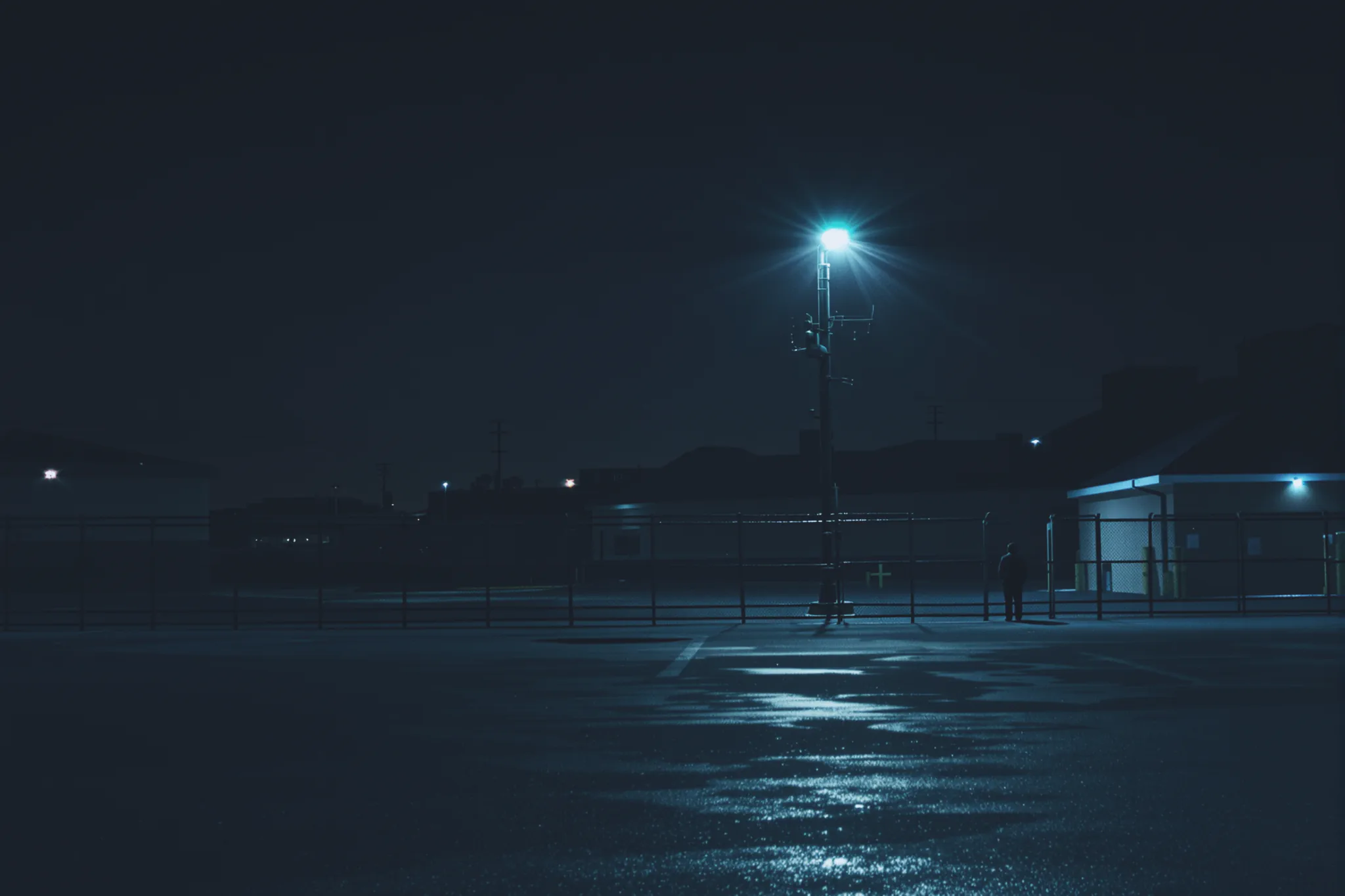 A retail loading dock at night with a single distant figure near the fence line.